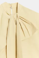 Camisa sin mangas confeccionada en algodón, con cuello redondo y detalle de lazada frontal. Presenta un diseño de corte holgado con bajo redondeado y cierre posterior mediante abertura y botones.