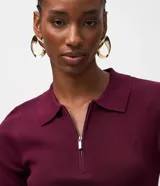 Blusa polo de punto color mostaza, ajustada al cuerpo, con cuello y manga corta. Presenta una cremallera frontal que llega hasta el escote.