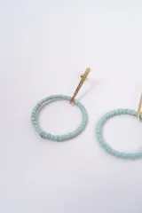 Aros colgantes con diseño circular, compuestos por un aro de fibra natural en color beige y una barra metálica superior con acabado texturizado.