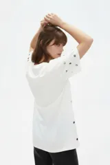 Remera holgada de manga corta y cuello redondo, color blanco, decorada con tachas plateadas distribuidas por toda la prenda.
