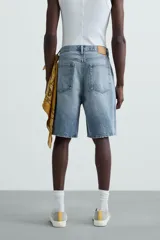 Bermuda de denim de algodón, color verde claro lavado, de corte recto y tiro medio. Presenta cinco bolsillos y cierre frontal con cremallera y botón.