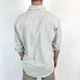 Camisa de manga larga a rayas verticales grises y blancas, con cuello italiano y logo bordado en el pecho.