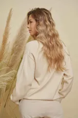 Buzo de punto color crema con diseño de corazones de colores aplicados en relieve, cuello redondo y mangas largas con puños acanalados.