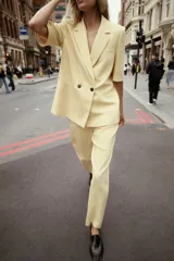 Blazer color amarillo pastel con textura, cuello solapa, manga corta con hombreras, bolsillos de vivo en delantero, forro interior y cierre frontal cruzado con botones.