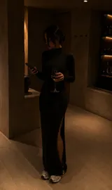 Vestido largo de corte ajustado, color negro, con cuello alto, mangas largas y una abertura lateral pronunciada en la falda.