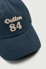 Gorra de seis paneles azul marino confeccionada en tejido de algodón, con bordado frontal en tono contrastante con la leyenda "button 84".