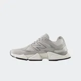 Championes urbanos New Balance modelo 9060, color gris con detalles en tonos más oscuros y claros. Presentan un diseño robusto con suela de plataforma esculpida, combinación de malla y superposiciones sintéticas, y el logo 'N' característico en el lateral.