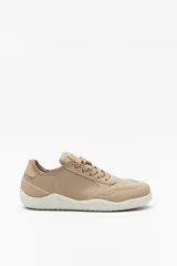 Zapatilla urbana de mujer color beige claro, de estilo minimalista y suela blanca gruesa. Presenta cordones a tono y paneles superpuestos de material liso.