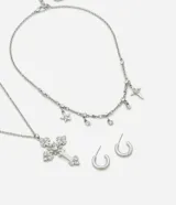 Conjunto de bisutería compuesto por dos collares y un par de aros tipo argolla. El primer collar presenta un dije de cruz ornamentado con cristales, mientras que el segundo es una gargantilla con dijes de estrellas y cristales. Los aros son argollas pequeñas de acabado liso.