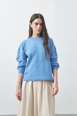 Sweater de tejido liviano con silueta relajada y hombro caído. Presenta cuello redondo, mangas largas con puños acanalados y lazos ajustables en el bajo.