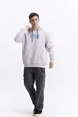 Canguro con capucha y cordones ajustables, confeccionado en algodón con detalle de estampado frontal en tonos verdes. Presenta un bolsillo tipo canguro delantero, puños y ruedo acanalados.