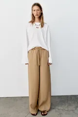Pantalón recto color beige de tiro medio, con cintura elástica, bolsillos delanteros y cinturón ajustable con hebilla metálica dorada.