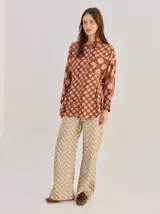 Camisa de algodón con estampado geométrico de ondas en tonos marrón y negro, corte holgado, mangas largas y cuello clásico.