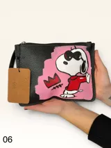 Sobre de cuero marrón con diseño pintado a mano que presenta al personaje Snoopy sobre un fondo rosado y la palabra 'heal'. Cuenta con cierre superior y etiqueta de cuero colgante.