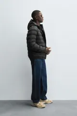 Campera puffer acolchada de corte regular fit en color negro, confeccionada en tejido técnico repelente al agua. Presenta cuello subido con capucha, cierre frontal de cremallera, mangas largas con puños elásticos y bolsillos laterales de vivo.