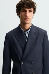 Blazer regular fit color azul marino, confeccionada en tejido con lana. Presenta cuello con solapas de pico, manga larga con puño abotonado, bolsillos de vivo en el pecho y de plastrón en la cadera. Incluye un bolsillo interior y aberturas en la espalda. El cierre es frontal con botonadura cruzada.