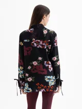 Camisa de seda color blanco con estampado floral y de dragones en tonos rojos, azules y verdes. Tiene cuello clásico, mangas largas con puños ajustables y botones forrados.