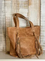 Cartera tipo tote bag de cuero color marrón, con diseño de doble asa y detalle de flecos largos en los laterales. Cuenta con un bolsillo frontal externo y costuras reforzadas.