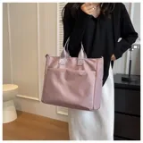 Bolso tipo tote color gris claro, con doble asa de mano y correa larga regulable. Tiene dos bolsillos laterales y un bolsillo frontal.