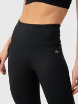 Calza deportiva de tiro alto con largo al tobillo, confeccionada con tecnología seamless para un ajuste suave y sin costuras. Presenta un diseño minimalista en color negro con logo sutil en la cadera.