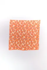 Pañuelo cuadrado de tela con estampado floral en tonos naranja y azul sobre fondo crema.
