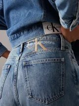 Pantalón de jean celeste de corte recto, tiro alto y pierna estrecha en el tobillo. Confeccionado en denim rígido de algodón y algodón reciclado. Diseño de cinco bolsillos y bragueta con cremallera. Logo de Calvin Klein bordado en la parte trasera de la cintura.