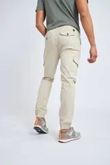Pantalón cargo color beige con ajuste slim, cierre frontal con botón, bolsillos laterales tipo cargo y puños elásticos en los tobillos.