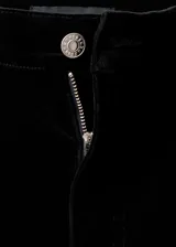 Pantalón de terciopelo negro de tiro medio y diseño wide leg con cinco bolsillos, cierre de botón y cremallera, y trabillas para cinturón.