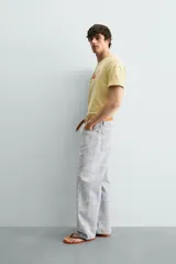 Camiseta de corte relajado color amarillo con efecto lavado. Presenta cuello redondo, mangas cortas con dobladillo y un estampado frontal con texto y un parche decorativo.