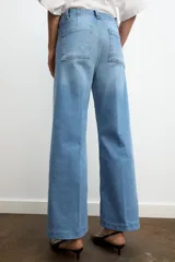 Jeans de tiro alto, pierna ancha y largo al tobillo, en denim celeste claro con efecto lavado. Presenta costura marcada en el centro de cada pierna y cierre frontal con cremallera y botón.