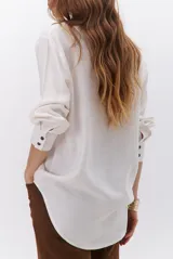 Camisa beige de manga larga con botones marrones y cuello clásico. Presenta un detalle de costura dorada a lo largo de la botonera.