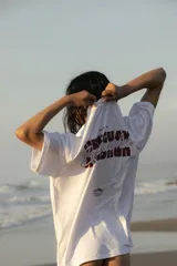 Remera blanca unisex de corte oversize, con mangas cortas y estampado en la espalda con la leyenda "Uruguay Biguá Beach" en color bordó.