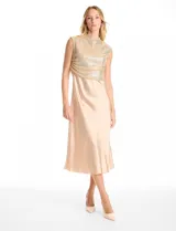 Vestido midi de satén color champagne con corte al bies y escote recto, acompañado por un top sin mangas de cuello alto cubierto de lentejuelas doradas con detalle drapeado en la cintura.