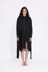 Vestido camisero negro de largo midi, con diseño asimétrico y efecto de capas. Presenta cuello clásico, cierre frontal de botones y mangas largas con puño. El bajo es irregular y deshilachado.
