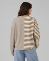Buzo oversize de corte asimétrico con diseño combinado de rayas verticales y horizontales en tonos beige y blanco. Presenta un corazón bordado en color celeste en el frente y una etiqueta decorativa en la manga.