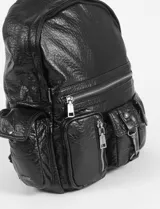 Mochila negra de cuero sintético con textura granulada, múltiples bolsillos frontales con cierres y broches, y tiras regulables.