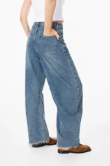 Jean de corte amplio y tiro medio, confeccionado en denim azul con acabado desgastado. Presenta un diseño de pierna curva tipo balloon, costuras horizontales en las rodillas y ruedo desflecado.