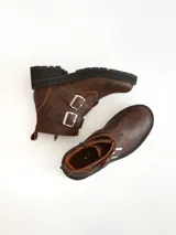 Botas cortas de cuero color marrón con suela track negra. Presentan dos correas ajustables con hebillas metálicas plateadas en el empeine y cierre lateral interno.