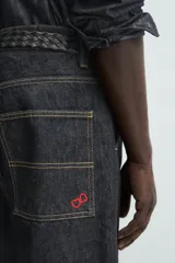 Pantalón chino de denim de algodón rígido, color índigo oscuro sin lavar. Corte baggy fit, tiro medio, con bolsillos frontales y traseros de plastrón. Presenta bordados a contraste en la cintura y en el bolsillo trasero.