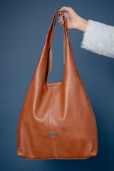 Bolso tipo tote de gamuza en color verde oliva, con diseño minimalista y asa integrada. Presenta una placa metálica con el logo de la marca en la parte inferior central y detalles de textura en el asa.