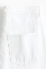Jean blanco de denim de algodón rígido, corte baggy con tiro alto, piernas holgadas de silueta curva y diseño de cinco bolsillos.