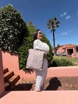 Bolso tipo tote bag de símil cuero color rosa pálido, con asas dobles y detalles de costura en color beige claro. Presenta un bolsillo frontal rectangular aplicado y herrajes metálicos.