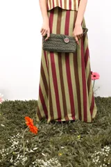 Bolso de mano tejido a crochet en trapillo grueso color verde oscuro, con un botón metálico grande y redondo con el logo de la marca CAPER en rojo.