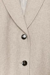Abrigo de paño color beige con cuello solapa, manga larga con hombreras y cierre frontal con botones. Presenta bolsillos delanteros de doble vivo y abertura en la espalda.