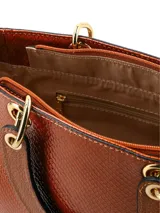 Cartera de mano de cuero sintético con acabado charol y textura de piel de reptil en color tostado. Cuenta con doble asa rígida superior, herrajes dorados y correa ajustable y removible.