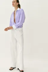 Camisa de popelín con diseño de rayas verticales en tonos blanco y lila, cuello solapa con escote en pico, manga larga y puños anchos contrastantes en color blanco. Cierre frontal con botones metálicos dorados.