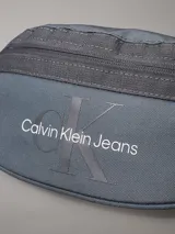 Riñonera Calvin Klein Jeans color gris oscuro con logo estampado en el frente, correa ajustable con hebilla y cierre superior con cremallera.