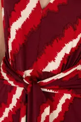 Vestido largo con estampado de rayas rojas, bordó y crema, con escote en V, mangas cortas y lazo en la cintura.