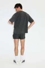 Remera deportiva de corte boxy y holgado con tecnología DryMove, en color gris oscuro con efecto gastado. Presenta hombros caídos, cuello redondo ribeteado y un gran estampado frontal en tonos claros con la palabra 'RUNNING' y siluetas de personas corriendo.