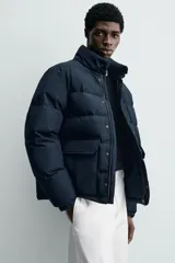 Campera puffer acolchada de corte regular fit, confeccionada en tejido técnico azul marino repelente al agua. Relleno interior de 80% plumón y 20% pluma. Cuenta con cuello subido, manga larga con puño elástico, bolsillos frontales de plastrón con solapa y cierre de cremallera oculta con solapa de botones a presión.